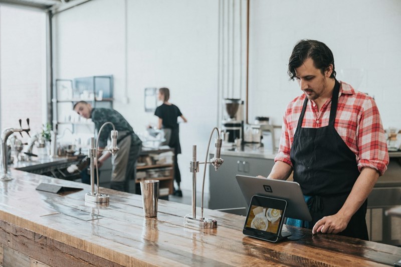 A barista uses a tablet at the cash register in a coffee shop