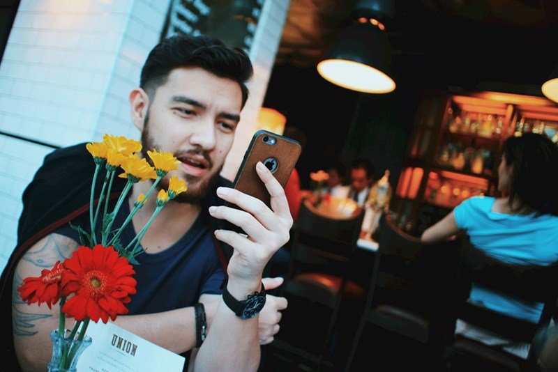 A man in a black tank top looks at his phone in a restaurant