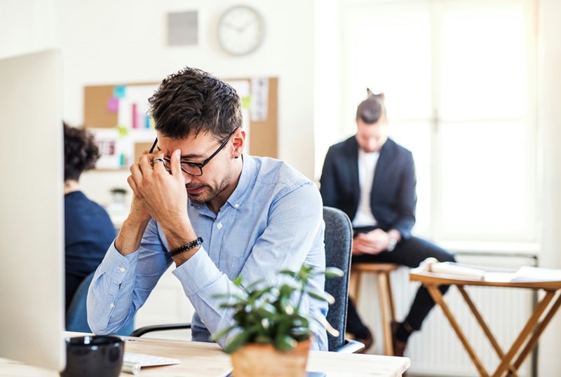 A frustrated young businessman puts his head in his hands at his desk
