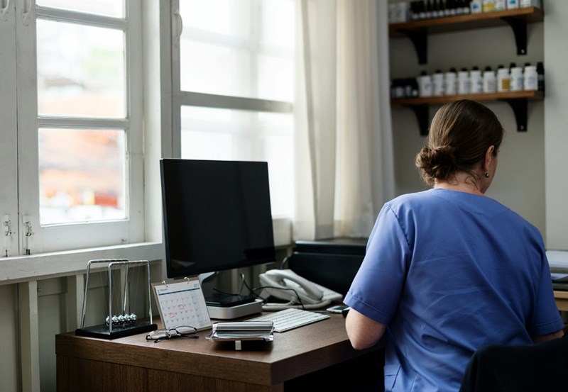 A hospital worker in blue scrubs works on a clipboard.
