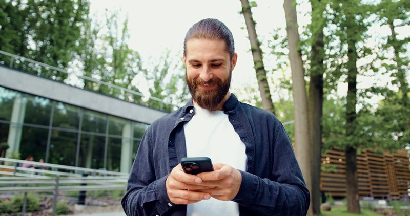 Bearded guy texting and smiles, standing out side with a satisfied look on his face