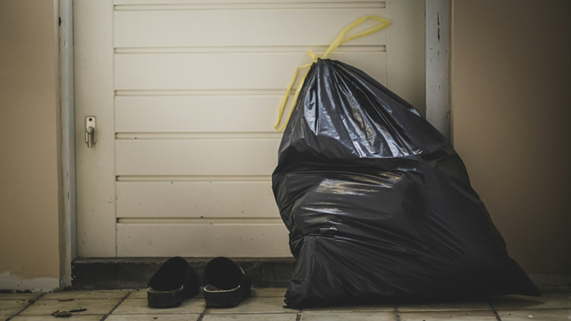 A full black trash bag and a pair of sliders sitting in front of an apartment door.