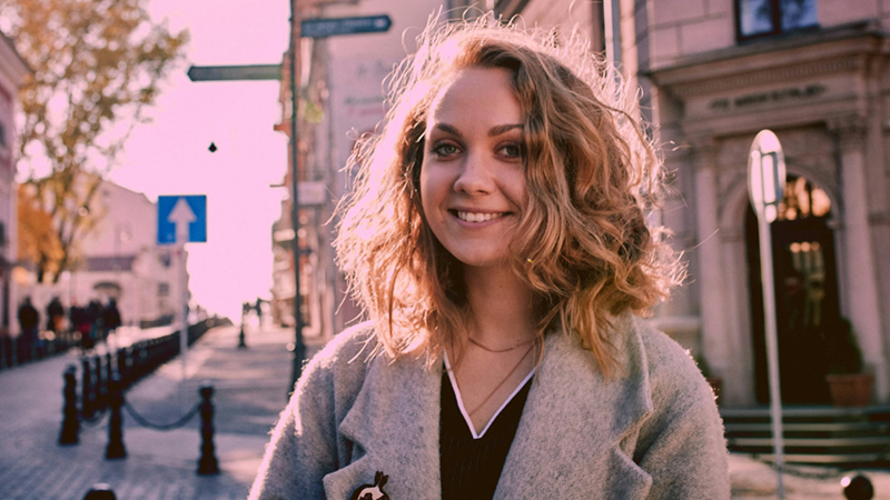 A young woman smiles as she stands in a city street.