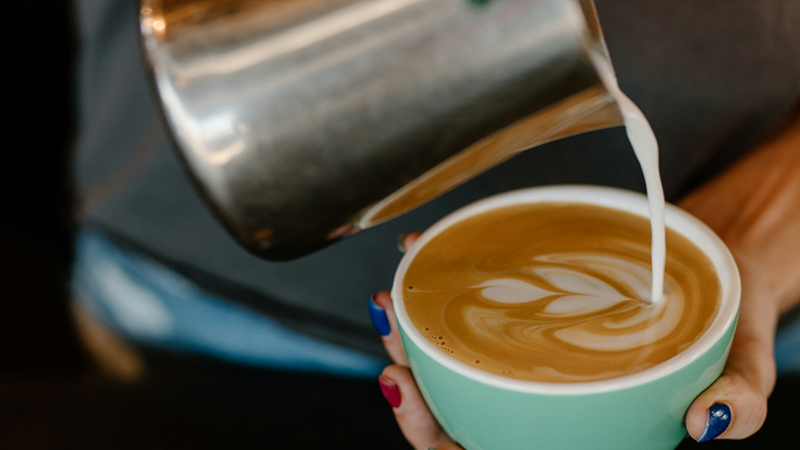 A close-up of a woman pouring frothed milk into her coffee.