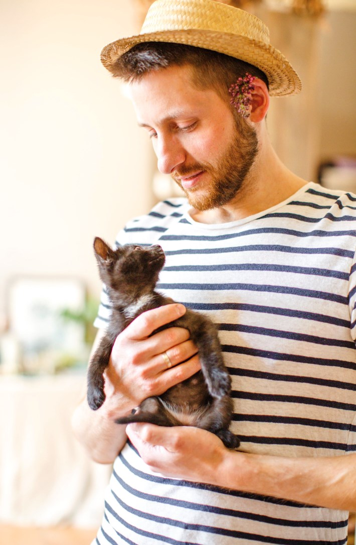 Man holds a black kitten against his chest.