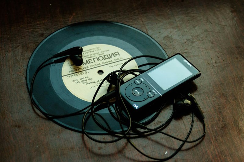 Portable MP3 player with wired headphones and a vinyl record.