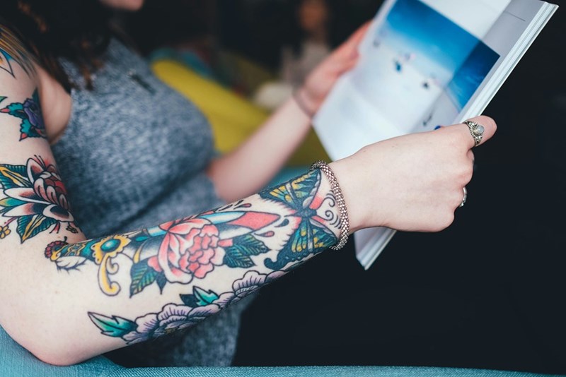 A woman reads a book with tattooed arms