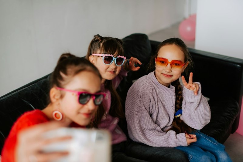 A group of Gen Alpha girls sit on a couch taking a photo