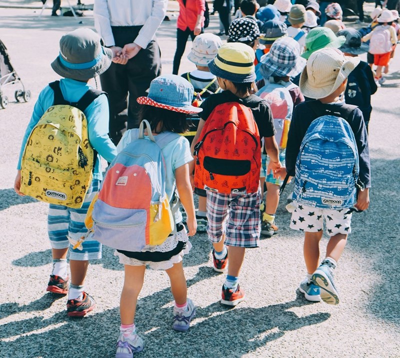 Group of kids wearing backpacks walking on pavement during daytime