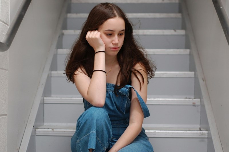 frustrated teen girl sitting alone on a staircase, resting her head on her hand