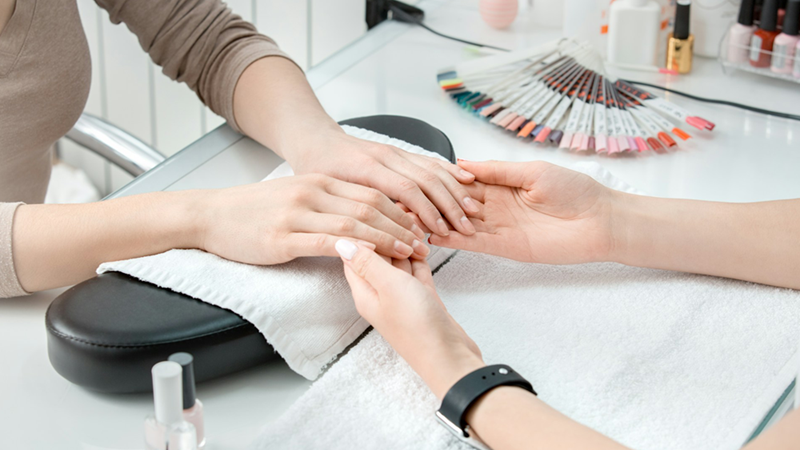 Close-up of a nail technician inspecting the hands of a client with nail color samples beside them.