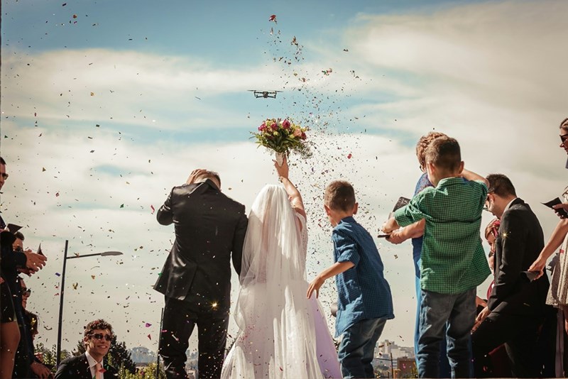 A groom stands beside bride about to throw a bouquet with young boys in the background
