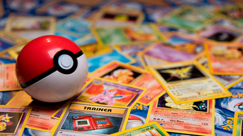 A pile of Pokémon trading cards with a Poké ball sitting on top of them.