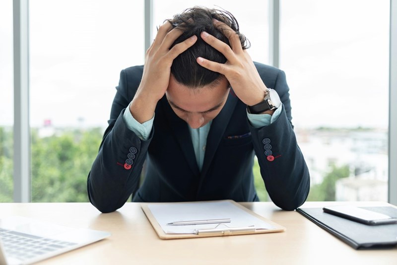Stressed corporate employee holding his head while sitting at his office desk.