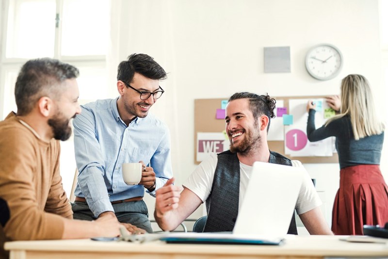 Cheerful coworkers laughing, representing the happy environment fostered by a colleague who shares free candy.