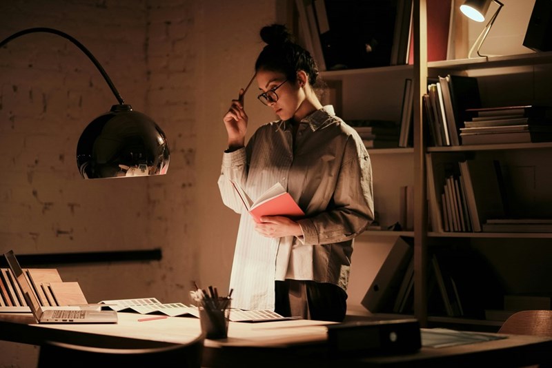 A woman scratches her head with a pencil at her desk