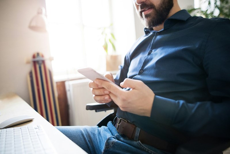 A man looks at his phone in his hands at a desk