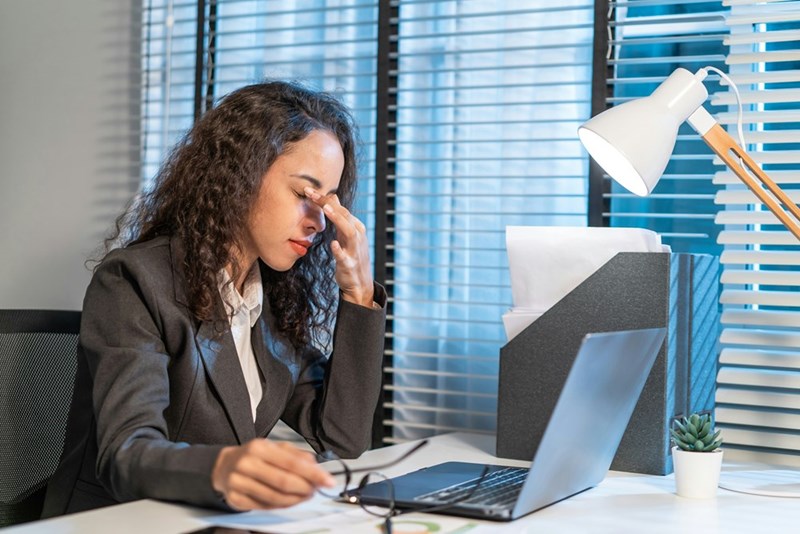 A worker massages her eyes while under a stressful workload