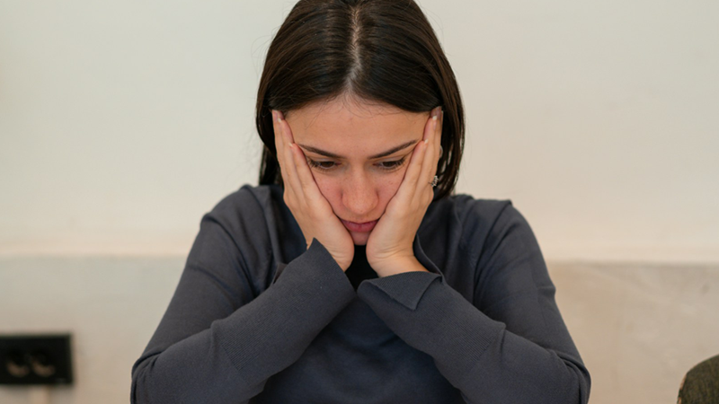 A woman sitting down with her hands on her face.