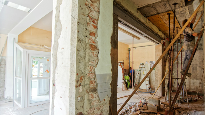 A workman on a ladder in a room with bare brick walls that is being renovated.