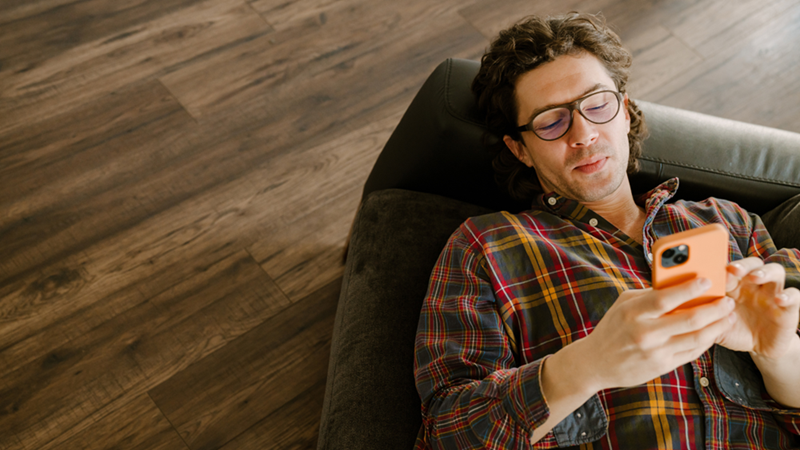 Man in plaid shirt lying on a couch using his smartphone looking content and pleased