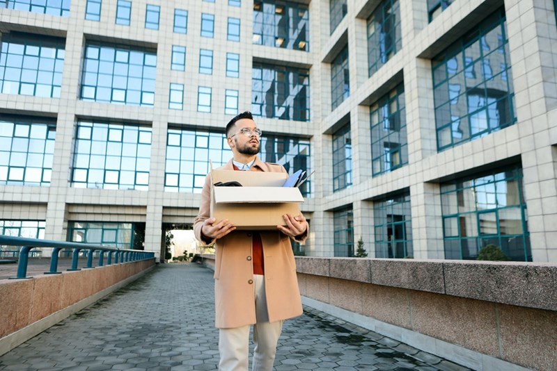 Employee leaving the office with a box of belongings after being fired by his company.