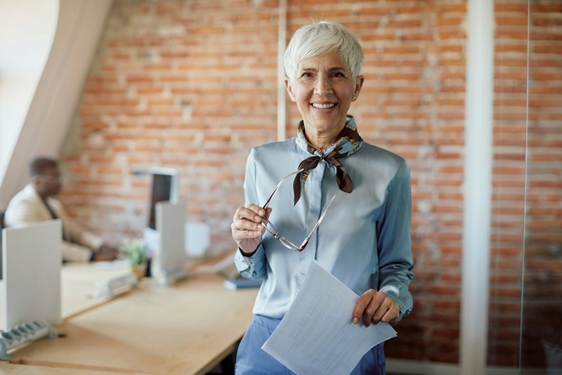Portrait of happy senior businesswoman working at corporate office and looking at camera