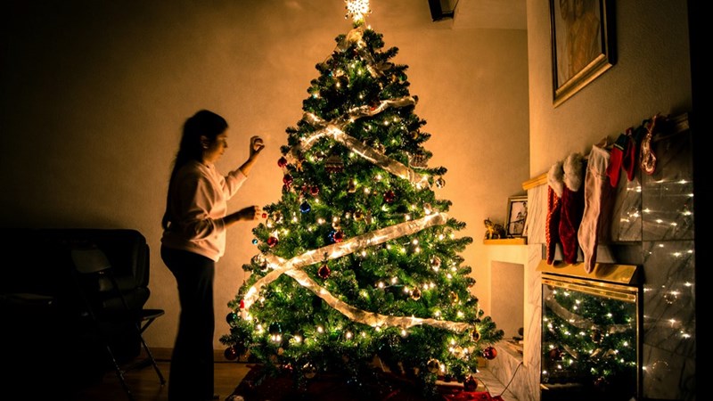 A woman decorating a christmas tree. Model portrayal.