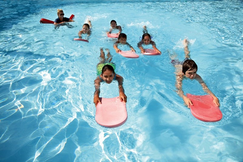 Children swimming together in the neighbor's pool during a birthday gathering.