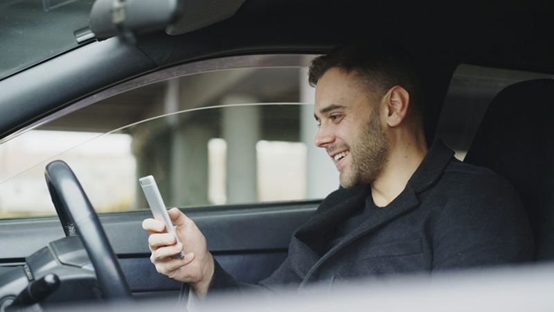 A man looking at his phone while sitting in the driver's seat of a car.