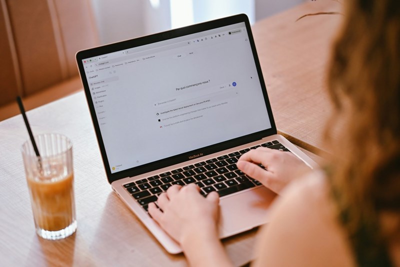 A person types at a laptop with iced coffee next to them