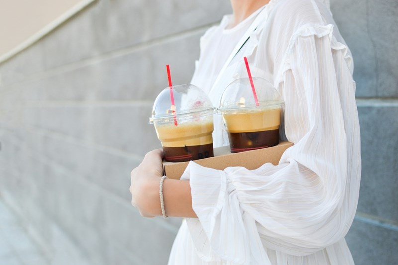 A woman carries iced coffee in disposable cups