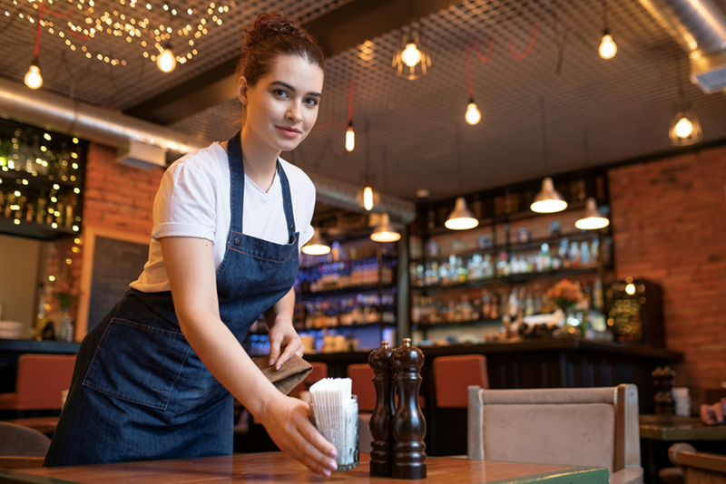 A young woman serves tables at her restaurant job