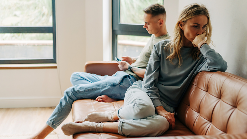 Man ignoring woman, while sitting on a couch. 