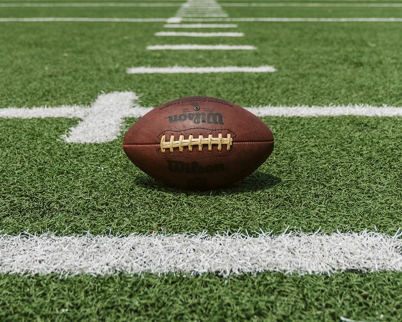 An American football rests on the field, illustrating the sport at the center of a neighbor dispute.