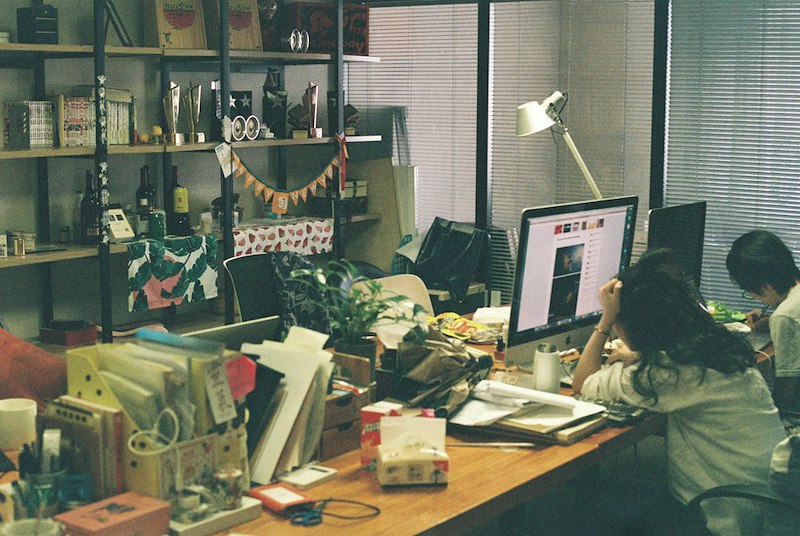 A cluttered desk at an office with tired workers at their desks