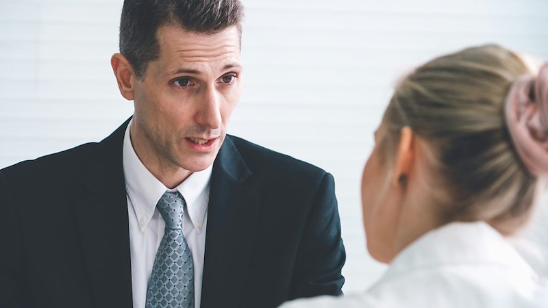 A man in a suit talks sternly to a female employee