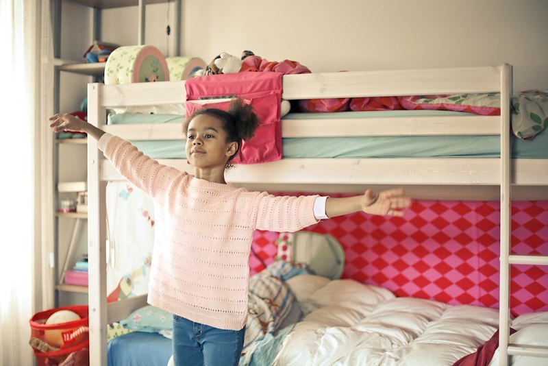 Girl in white and red long sleeve shirt and blue denim jeans near bed