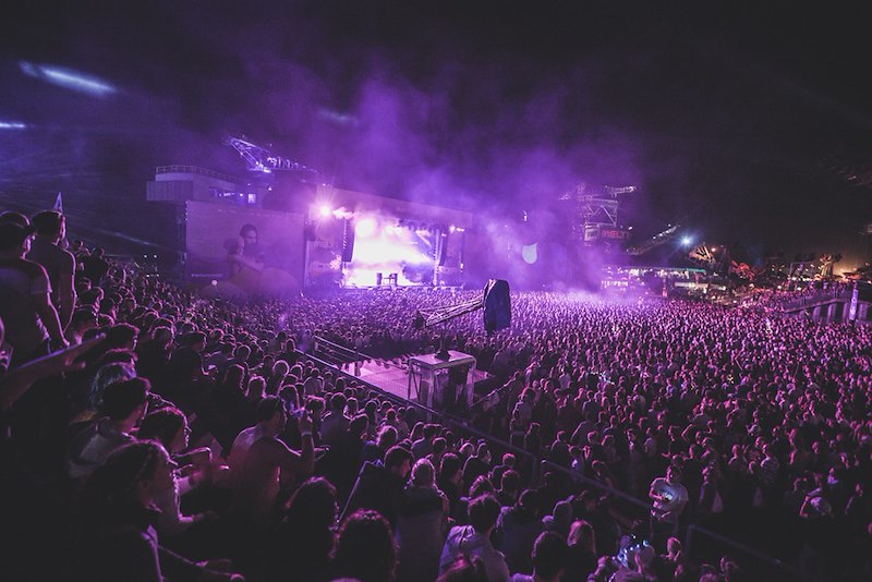 A packed concert venue with a distant view of the stage, showing seating differences.