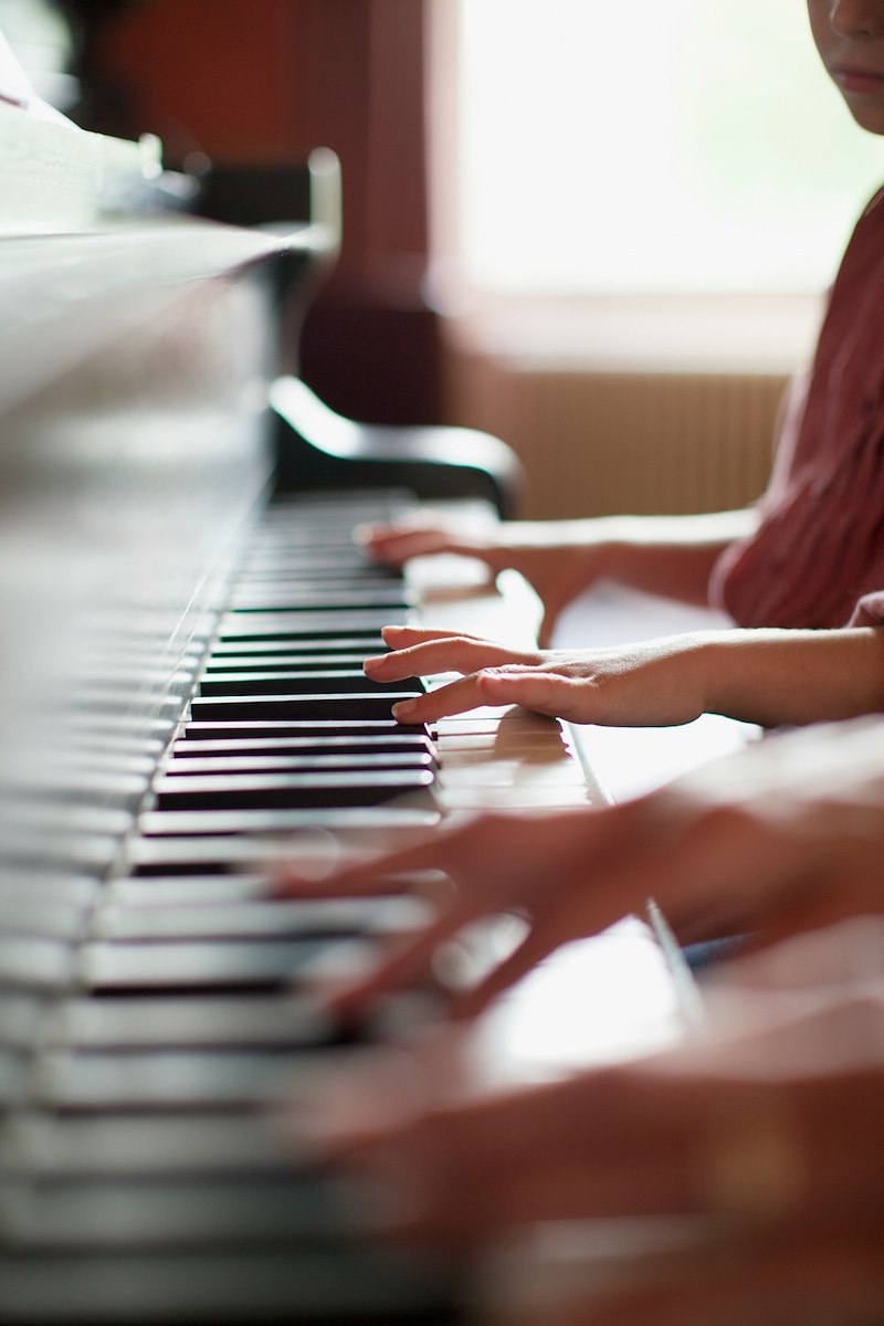 A young piano student plays piano with her teacher during a lesson.