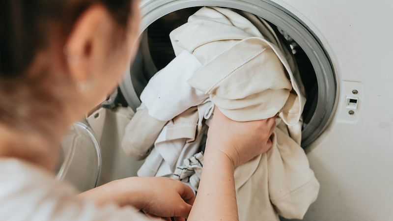 Close-up of a woman putting laundry in a washing machine.