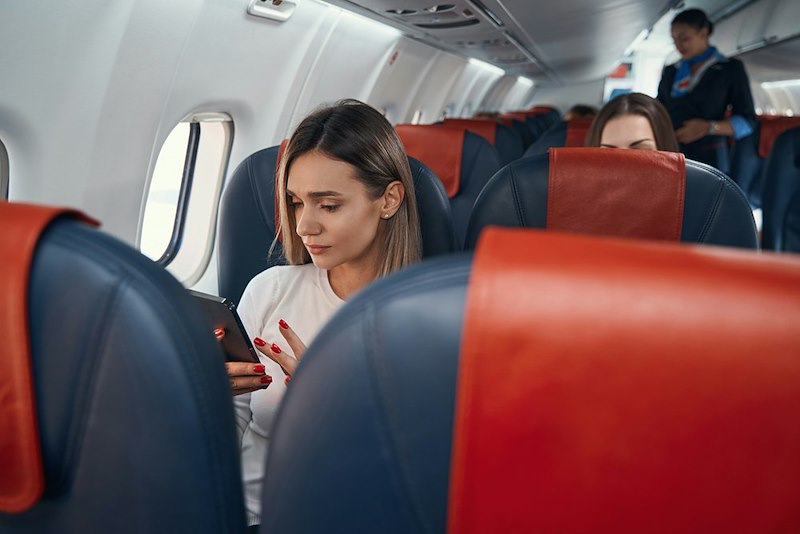 A woman in an airplane seat looks at her phone