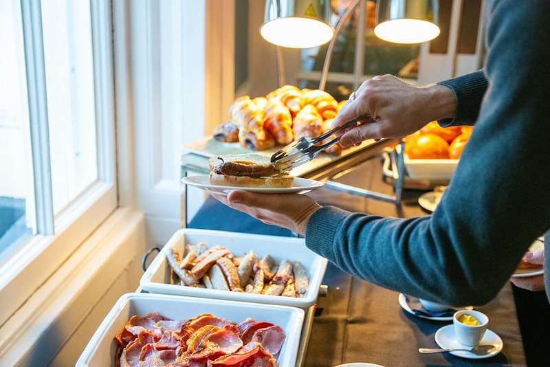 A person serving his plate with food from the breakfast buffet.