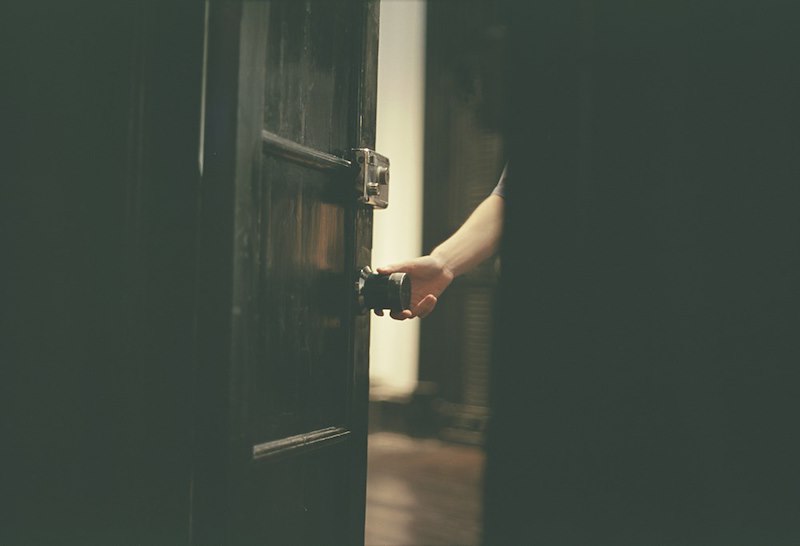 A hand opens a door in a dark hallway