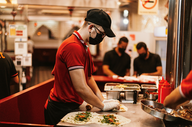 A man with a mask on prepares food at a fast food restaurant