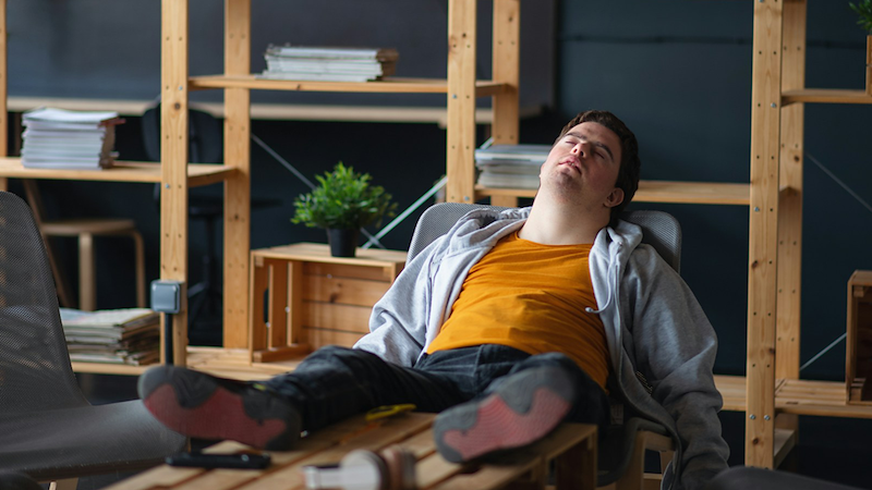 A man lounges on a chair with his feet on a coffee table in front of him.