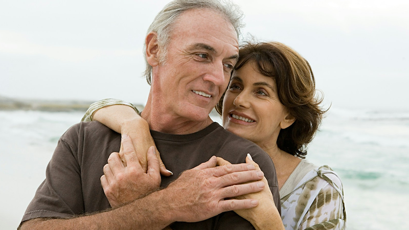 A woman embraces a man from behind in front of a body of water.