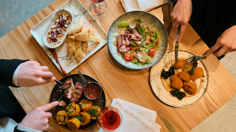 Overhead view of diners beginning to eat several dishes at a table.