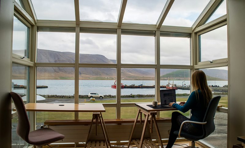 A remote worker sits at a chair in front of a window