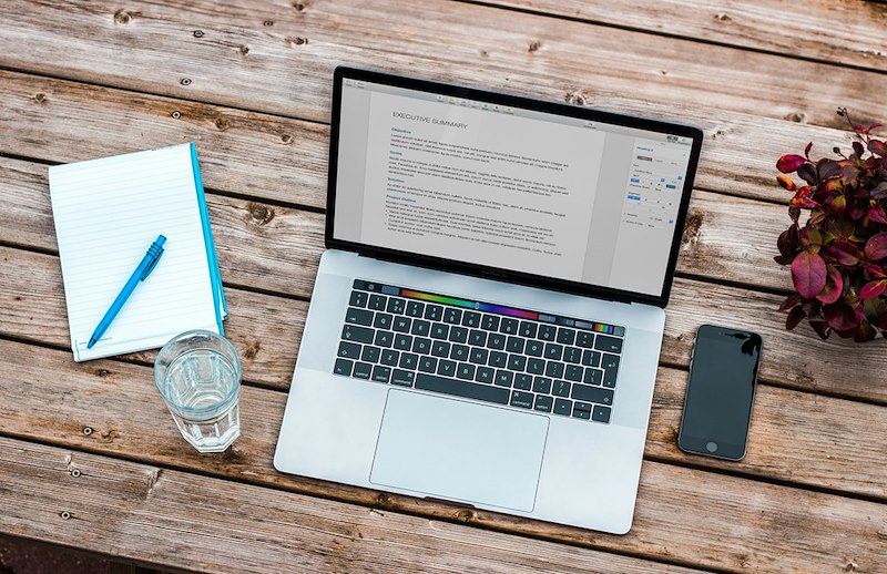 A computer, a notepad, a pen, and a cellphone on a table.